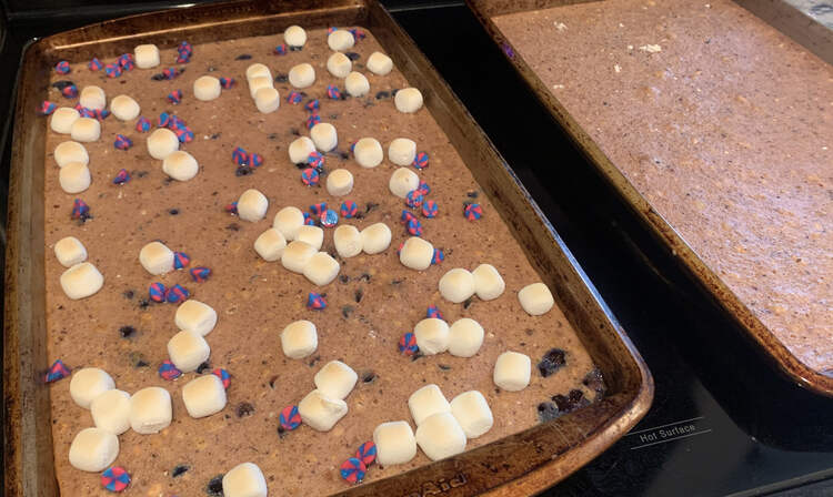 Image shows two sheets of blue tinted pancakes. The ones on the right are plain while the ones on the left show browned ballooned marshmallows and unicorn swirled chocolate chips.