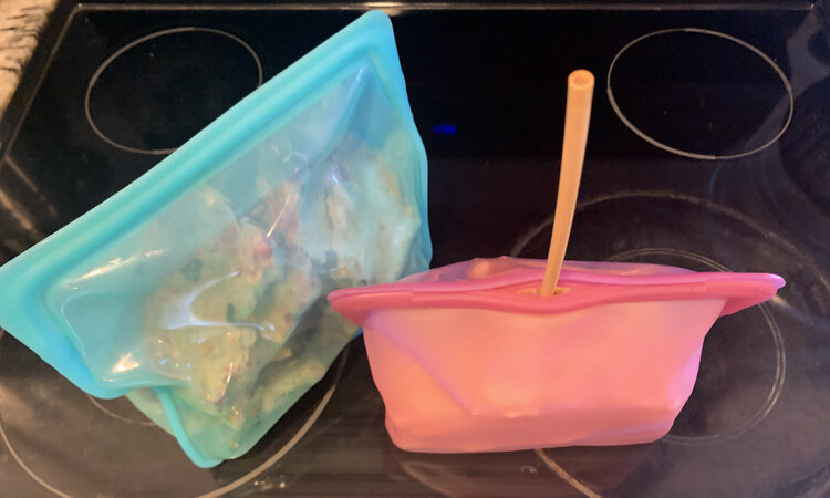 Image shows two Stasher bags side by side. The one on the left is sealed while the one on the right is mostly sealed with a straw sticking out of it. 