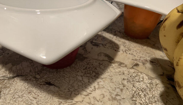 Image shows two plastic cups with pantry stable foods covered with a saucer so they stay safe overnight. To the right you can spot a bunch of bananas ready to grab. 