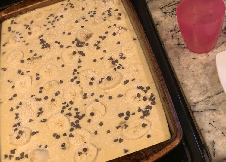 The pink cup is now emptied and the pan shows the bananas and dough coated in mini chocolate chips and white flecks of coconut. 