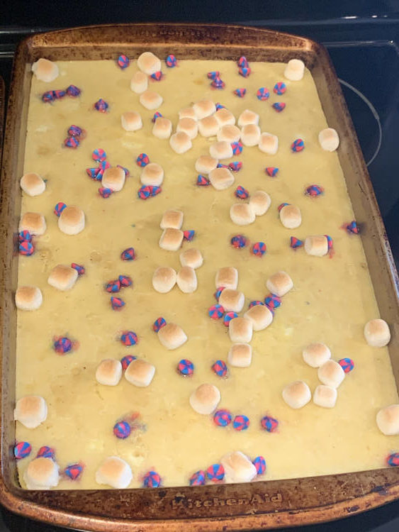 Image shows a single sheet pan containing a baked pancake covered in pink and blue swirled chocolate chips and browned inflated mini chocolate chips. 