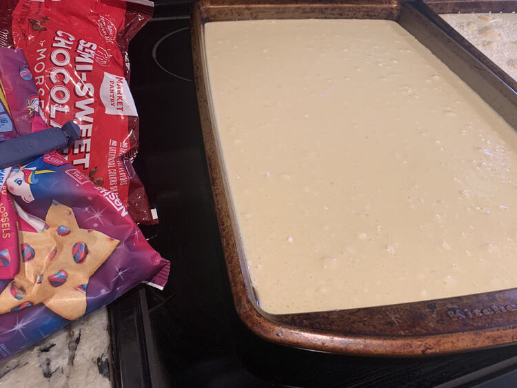 Image shows an plain batch of pancakes in a cookie sheet with the previous pina colada one off to the side. On the other side are two packages of chocolate chips ready to be sprinkled on. 