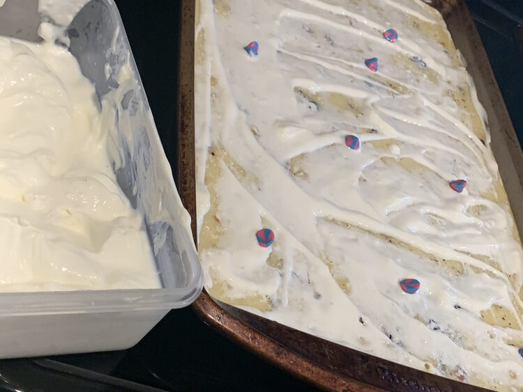 Image shows a sheet pan with white labneh spread all over it and the odd pink and blue swirled chocolate chip on top. To the left is a container of more labneh. 