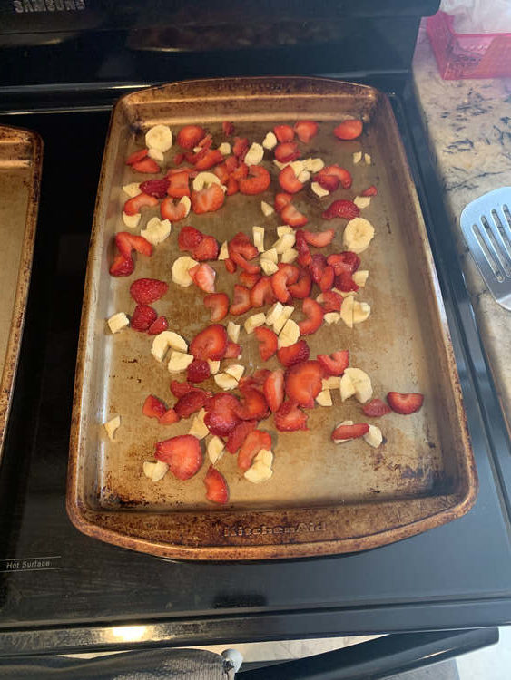 Image shows a closeup of a sheet pan covered in red strawberries and white-ish banana chunks.
