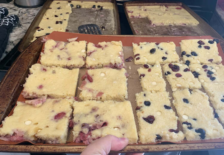 Image shows a Silpat lined cookie sheet with two types of pancakes lined up on it. In the background are two other half emptied sheets holding the fresh pancakes from the oven. 