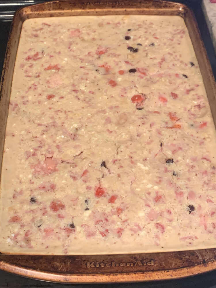 Image is a closeup of a single cookie sheet containing beige batter with chunks of red and pink (strawberry) and the odd chunk of brown (chocolate chip). 