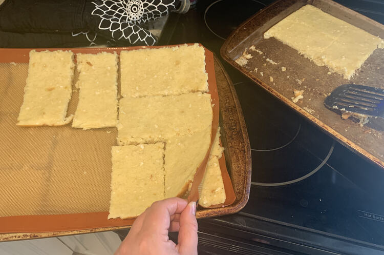 Image shows the cookie sheet with one full layers of pancakes on the bottom and a partly filled layer at the top. I'm lifting a corner to better see below. Off to the side you can see a cookie sheet with only six pieces left. 