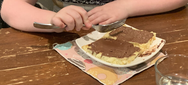 Image shows two pancakes side by side on a square saucer and a fork poised above about to cut a piece. 