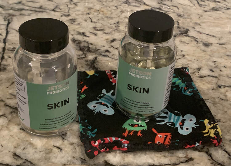 Image shows two green "skin" probiotic bottles sitting on the counter. The right one sits on a black monster adorned napkin while the left one sits on the bare counter. 