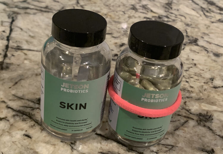 Like the before photo this one shows two bottles sitting on the counter. This time there's no napkin underneath either of them and the right one has a pink ponytail tie around it's center. 