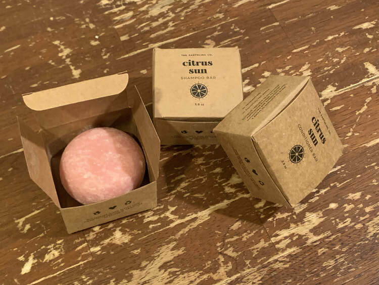 Image shows three boxes containing two shampoos and one conditioner bar. The left one is opened showing a white dappled pink bar while the shampoo and conditioner bar beside it are closed so you can't see it. 
