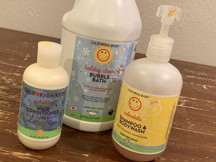 Image shows a half gallon jug of holiday cheer! bubble bath with a pump bottle of calendula shampoo and bodywash to the right and a small hair conditioner to the left.