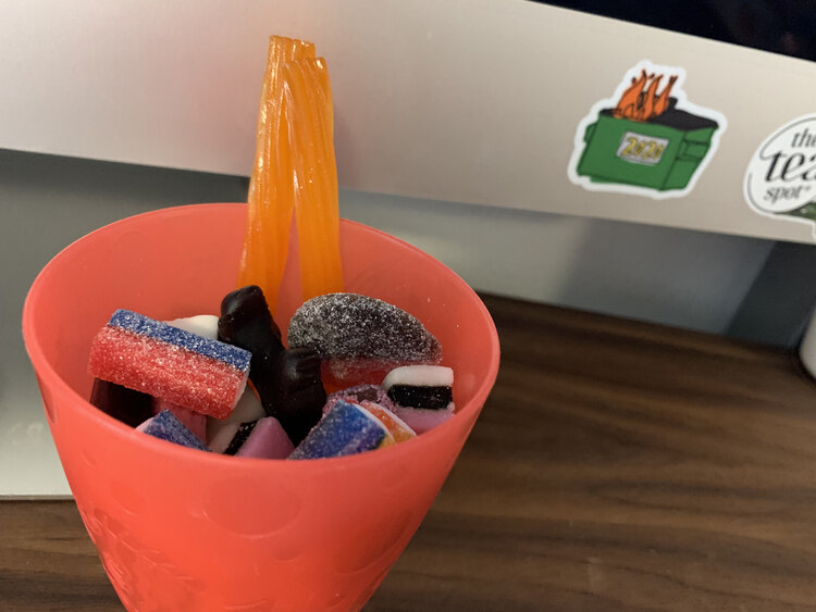 Image shows a closeup of a red plastic cup filled with an assortment of licorice in front of my computer.