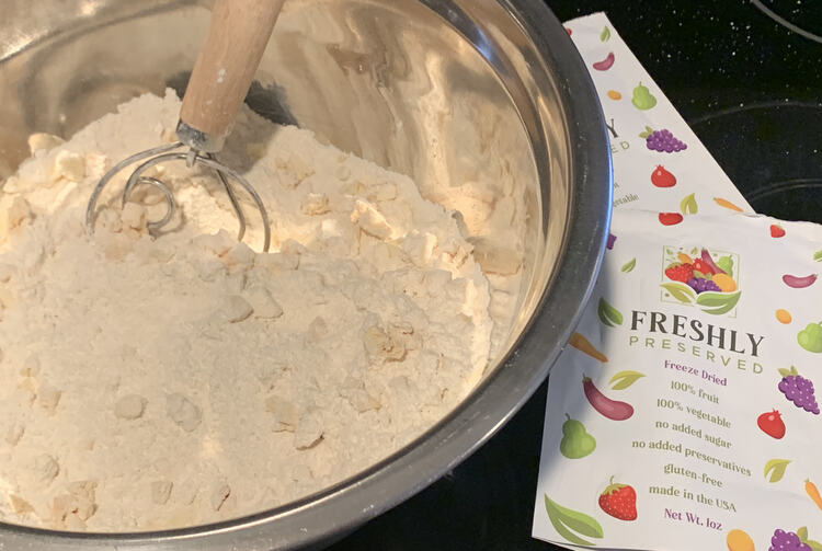 Image shows a closeup looking down into a bowl with dried ingredients (flour-like) with chunks of white in it. Beside the bowl are two bags labeled "Freshly Preserved"