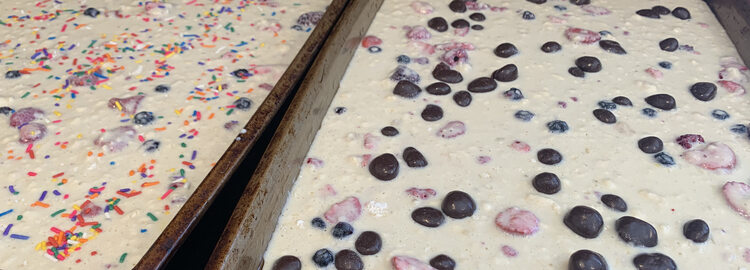Two sheet pans side by side. The left one is covered in multicolored sprinkles while the right one has large dark circular lumps mixed in with the red strawberries. 