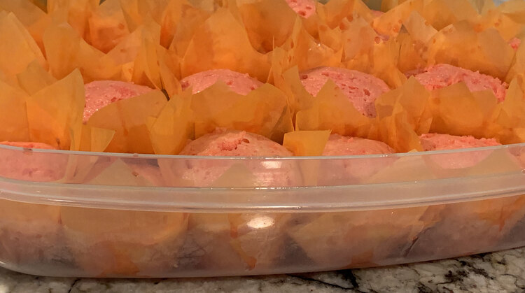 Image shows the clear container from the side so you can see the pink liquid pooling in areas and the top of the pink cupcakes above. There's pink Jell-O drippings on the top of the orange cupcake liners too.