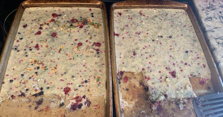 Image is taken of the same view but further away making the blueberry in the pancakes more visible. The bottom bit of both pans have been dished with a metal flipper placed to the side. 