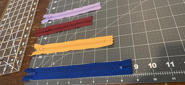 Image shows the zippers lined up on a quilting cutting board showing each of their length. 