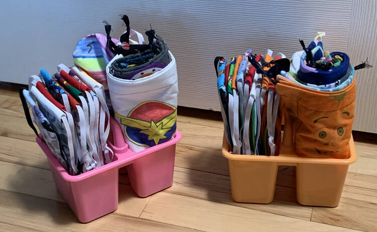 Image shows two plastic Dollar Tree containers each containing new fabric masks, two zippered pouches, and ten ribbon cinched bags.