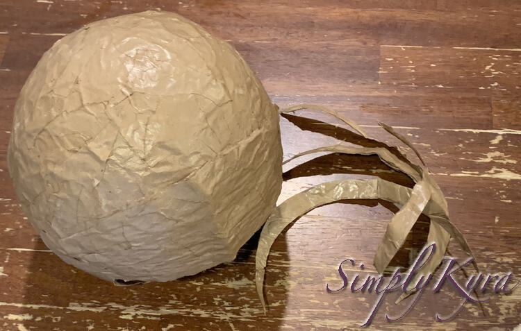 Image is taken from above looking down at the top of the helmet resting on the kitchen table. To the right are many long slivers of paper mache that had been trimmed off of the back of the helmet. 