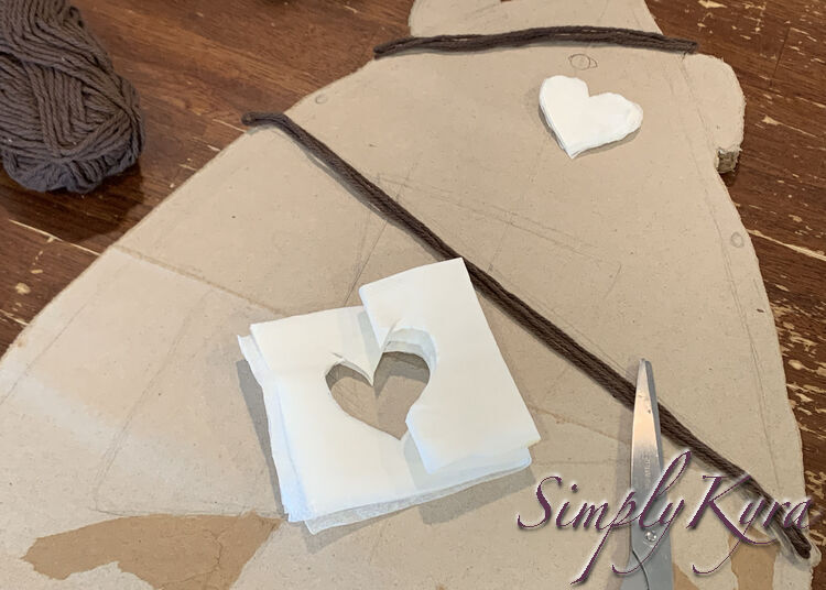 Image shows the skateboard with a small stack of heart shaped napkin layers placed next to the ink-marked circle. Near the bottom of the photo you can see the scissors and the rest of the napkin with the heart cut from the center. 