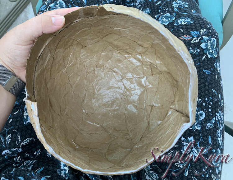 Image shows me holding the helmet upside down in my lap. The raw edges, for lack of a better term, are mostly white showing where I had just applied the Mod Podge.