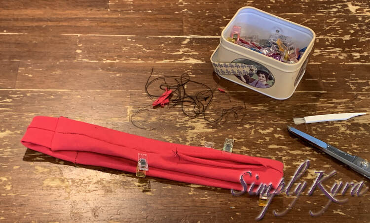 Image shows me the final loop right side out with the opening gapping open as the raw edge is curling. The center lengthwise seam is centered on the flattened band with sewing clips keeping the proper edge folded.