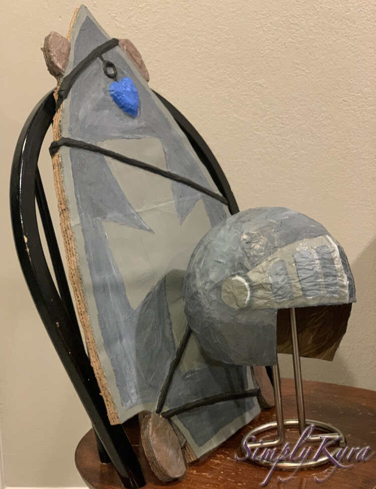 Image shows both items on a kitchen chair. The skateboard is upright leaning against the chair's back. The helmet is on a metal paper towel stand resting in front of the skateboard. 