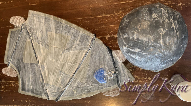 Image shows the top side of the skateboard beside the helmet. Both are coated in white streaks of Mod Podge but have the painted color showing through underneath.