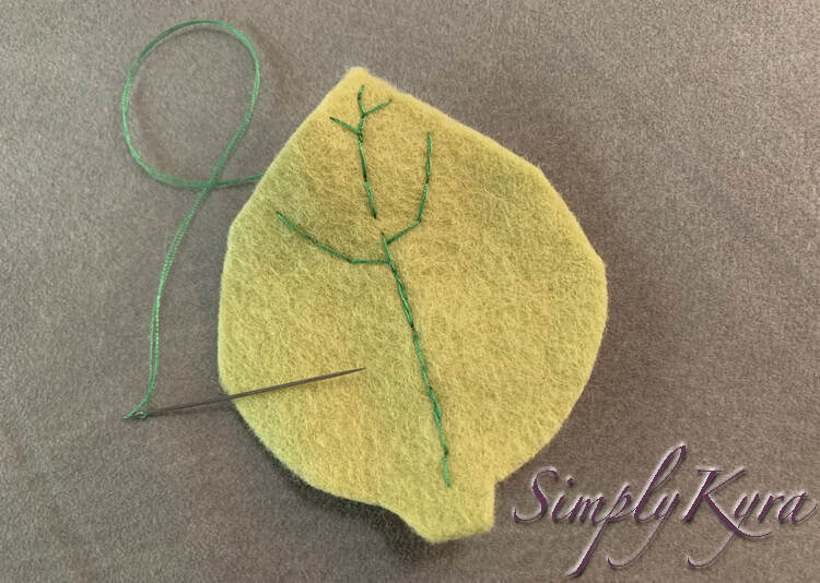 Image shows a single light green felt leaf with a threaded vein going up the center with two branches near the top and two smaller ones at the top. The needle is placed overlapping with the edge and the thread is going back under the leaf so you can't tell exactly where I was working. 