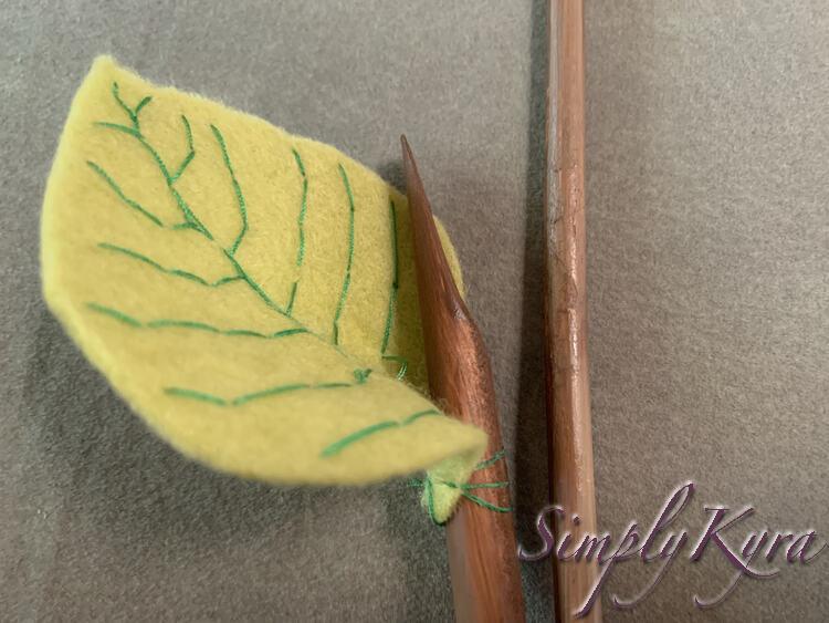 Image shows the leaf attached at the base to the brown branch with green threads. The sides and top of the leaf curl naturally away from the branch. 