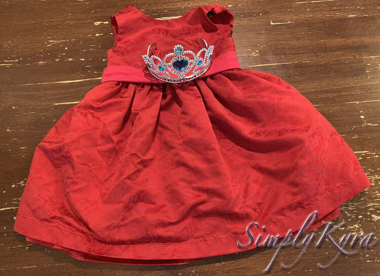 Image shows the red dress with the pink band carefully laid out so the silver is hidden. The blue crown is placed over the pink sash.