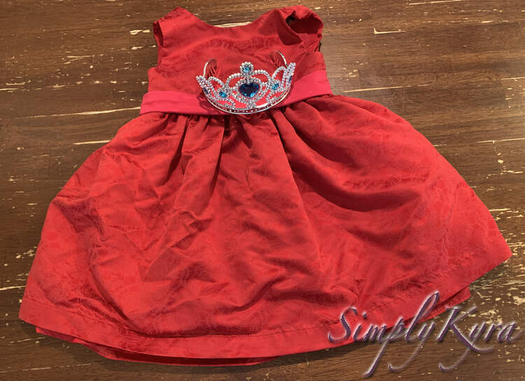 Image shows the red dress with the pink band carefully laid out so the silver is hidden. The blue crown is placed over the pink sash. 