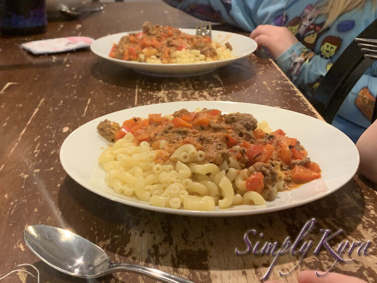 Image shows the kids sitting and eating from their white plates with macaroni and the meat sauce. One is closer to the camera and the other is a bit further back. 