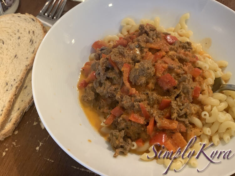 Image shows a bowl with pasta and meat sauce on top. A fork and spoon rest to the left of the bowl with two rye pieces of toast resting on top. 