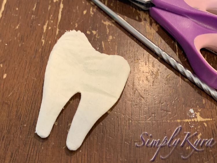 Image shows a white tooth with sewn smoothed edges along most of it. The top left corner is raw with thread showing where the opening is located. Off to the top right side yo can see the handle of the pinking shears and the metal chopstick.  