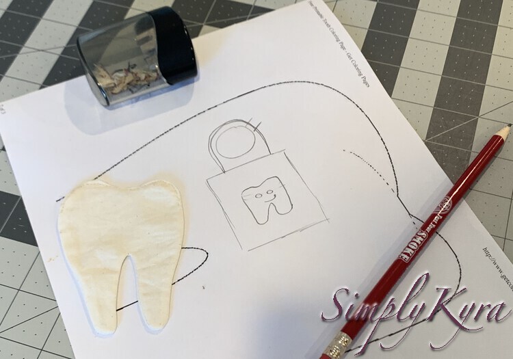 Image shows an extra large tooth printout with my quick sketch doodled in the blank center. To the top is a used pencil sharpener, to the left the white finished tooth, and to the bottom a pencil. 