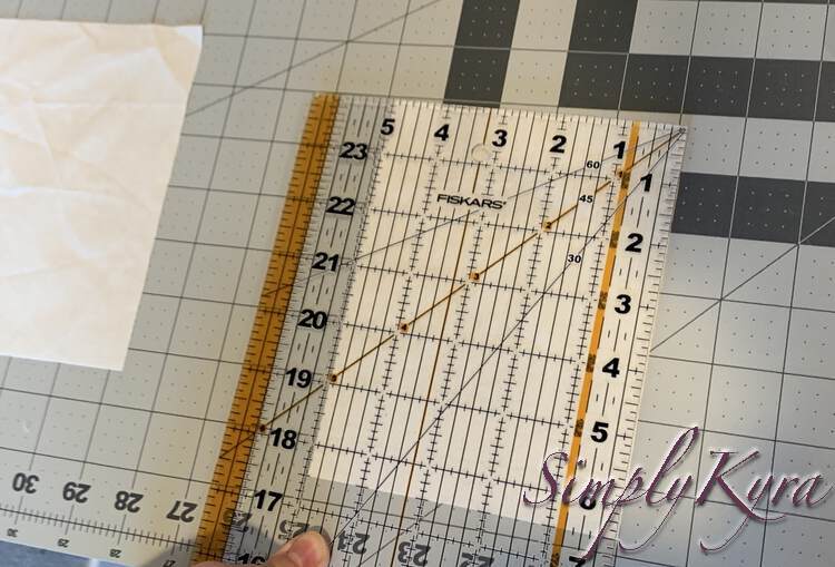 Image shows a transparent marked quilting ruler laid out over a rectangle of white fabric. You can see it measures 5 inches by 6.5 inches. Another matching rectangle of white fabric is off to the side. 