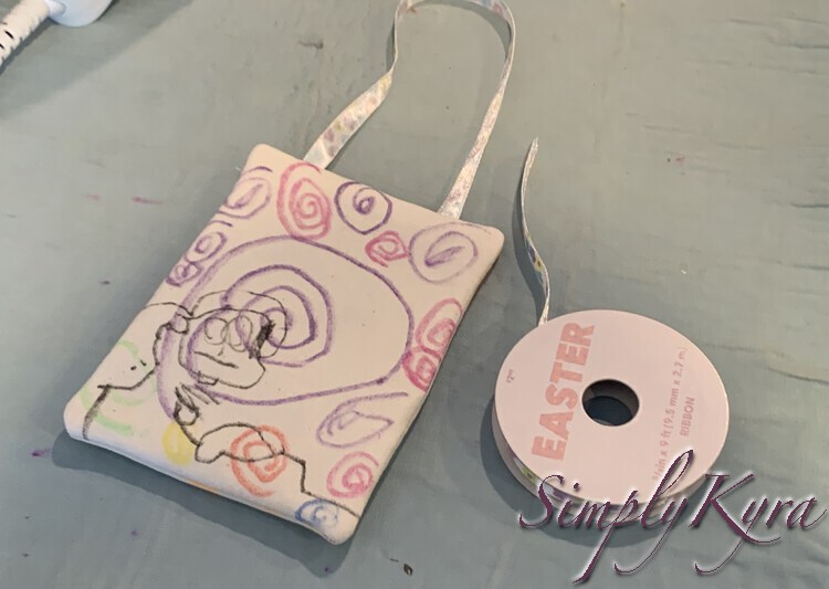 Image shows the back of Ada's tooth fairy door hanging with a flowered ribbon coming out of the top. The original roll of ribbon is beside and labelled: Easter.