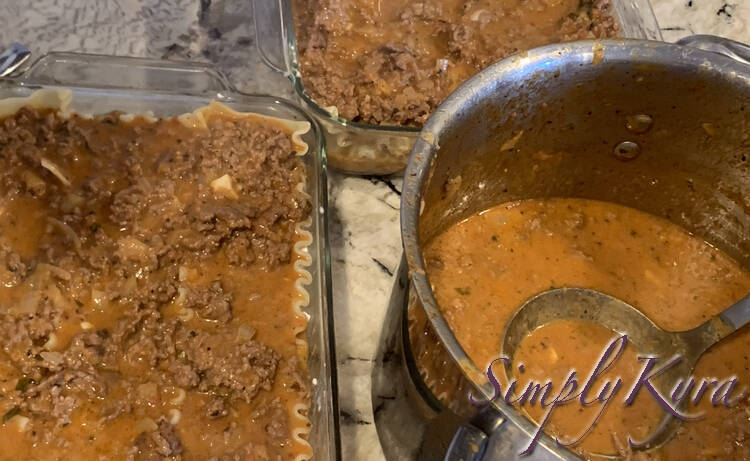 Image shows a large pot of meat sauce with a soup ladle in it to the right. To the left is a mostly filled 9 by 13 inch glass casserole dish and in the back is a mostly filled 8 by 8 dish. 