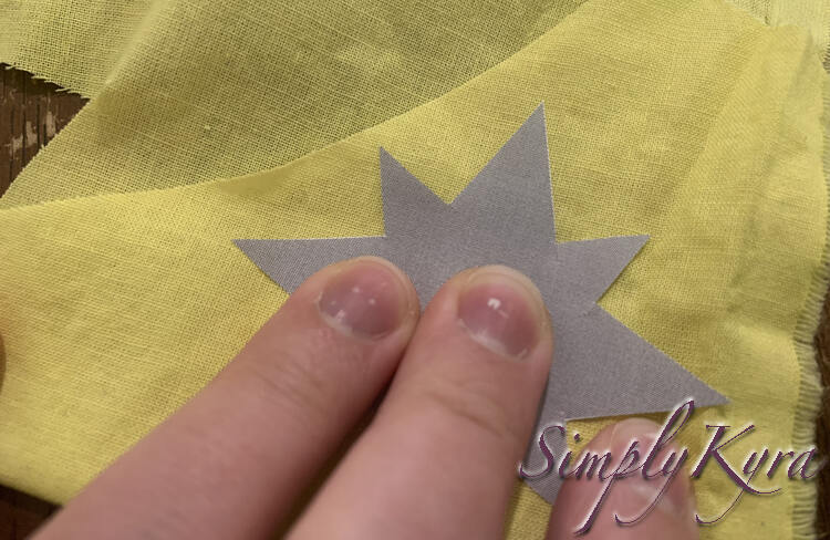 Image shows me pressing some fingers down on the grey star placed on top of the two-layered yellow fabric. 