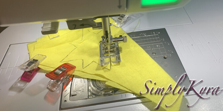 Image shows the scrap of yellow fabric in my sewing machine with four sewing clips still attached. The needle is in the outline and yellow thread is traced along it's length as it's fed to the needle point.