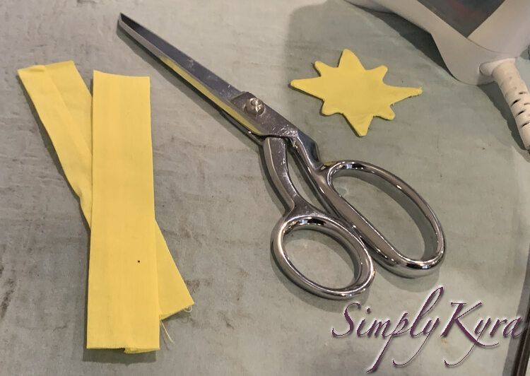 Image shows two six inch long strips of yellow fabric, a pair of metal fabric scissors, and a yellow eight point star. 