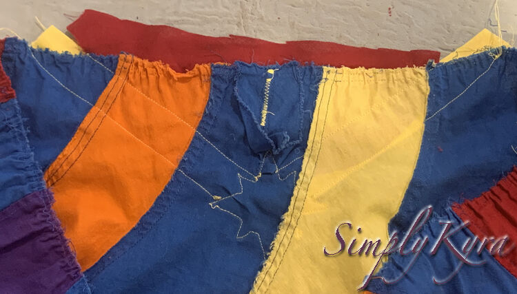 Image shows the back side of the skirt's front (previously dress back). Here you can see the blue facing, bunched at the bottom, along with the yellow zigzag stitch, at the slit, and along the star and strips' edges. 