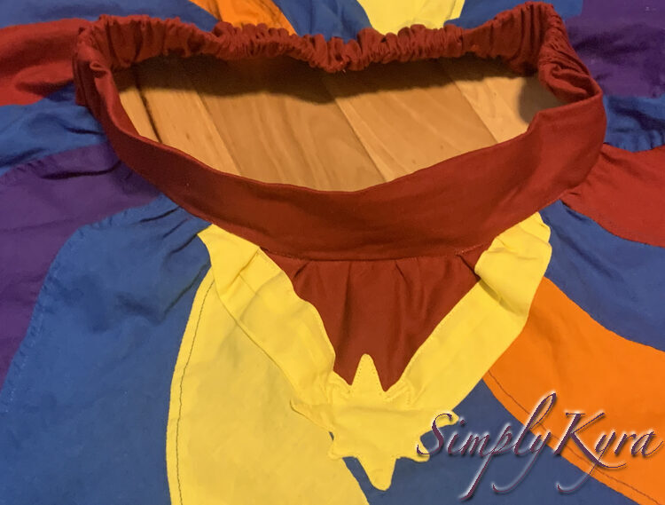 Image shows a flat lay of the skirt with the entire emblem at the bottom, the open waistband in the upper half, and the skirt swirls reaching out. The photo is cropped to not show the excess swirls. 