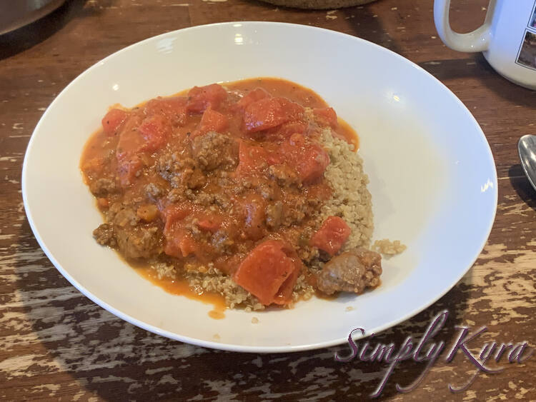 A white bowl with a mound of quinoa sits topped in ground beef, diced tomatoes, and tomato soup leftover sauce.
