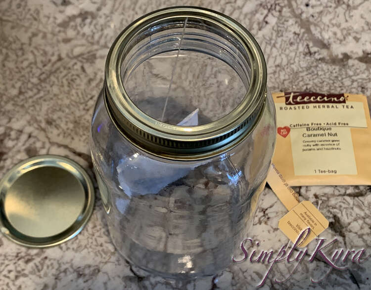 Image is taken from above, at an angle, showing the canning jar with the outer ring on and the teabag hanging from it where the string is caught. To the left is the inner section of the lid and to the right you can see the emptied tea bag package and the tag with a string sticking out. 