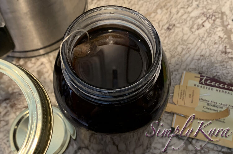 Image is once again taken from above looking down at the canning jar. The lid is lifted up, shown on bottom left, with the inner lid blurred below. The string is stuck to the rim of the jar and the teabag floats below. 