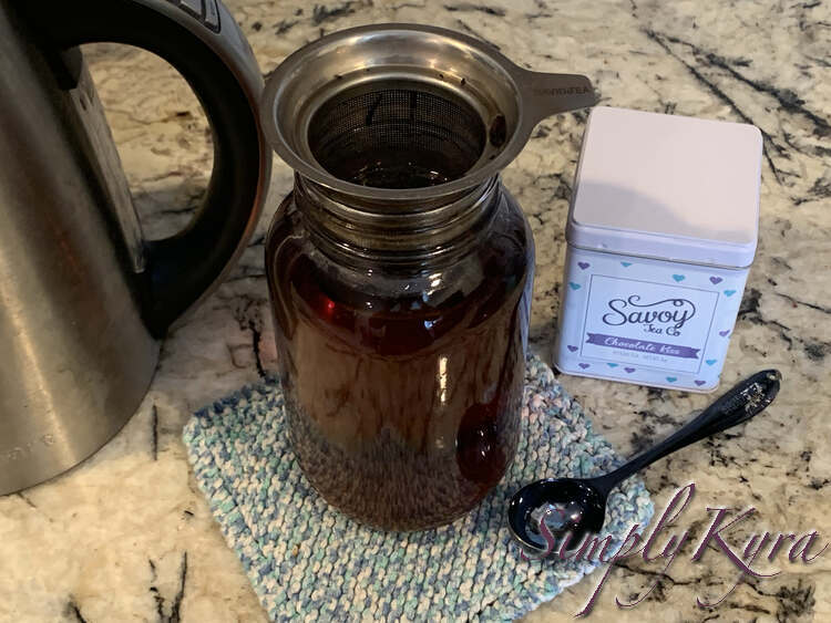 Image shows the canning jar filled with tinted water with the infuser placed on top steeping it further. Underneath it sits a blue and white speckled knitted dishcloth. 