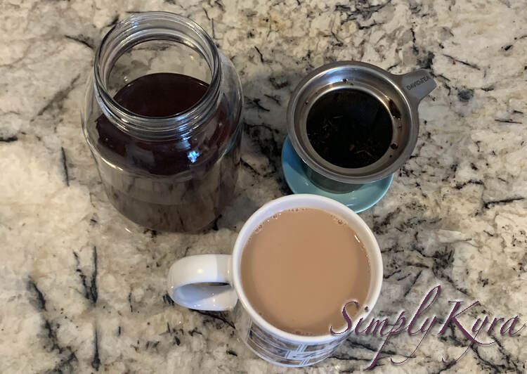 Image shows an image taken from above. You can see the half filled canning jar, with dark liquid, to the left. To the right sits the used tea in the infuser on a blue dish. At the bottom is my mug filled with light brown tea. 